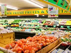 Grocery store produce section with bagged onions in wooden bins, shelves of fruit and vegetables, and hanging signs offering 50% off fruits and veggies