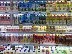 Supermarket dairy case stacked with cartons and jugs of fresh, low-fat and chocolate milk, with yellow price tags on the shelves
