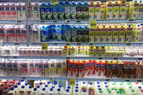 Supermarket dairy case stacked with cartons and jugs of fresh, low-fat and chocolate milk, with yellow price tags on the shelves