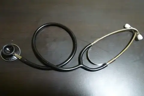 A stethoscope with black tubing looped in a circle and metal ear tubes with white ear tips, lying on a dark wooden table