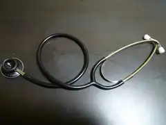 A stethoscope with black tubing looped in a circle and metal ear tubes with white ear tips, lying on a dark wooden table