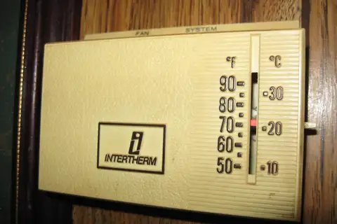 A beige Intertherm mechanical wall thermostat with a Fahrenheit and Celsius scale and a red setting marker near 70 degrees, mounted on wood paneling
