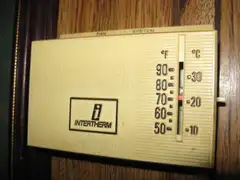 A beige Intertherm mechanical wall thermostat with a Fahrenheit and Celsius scale and a red setting marker near 70 degrees, mounted on wood paneling